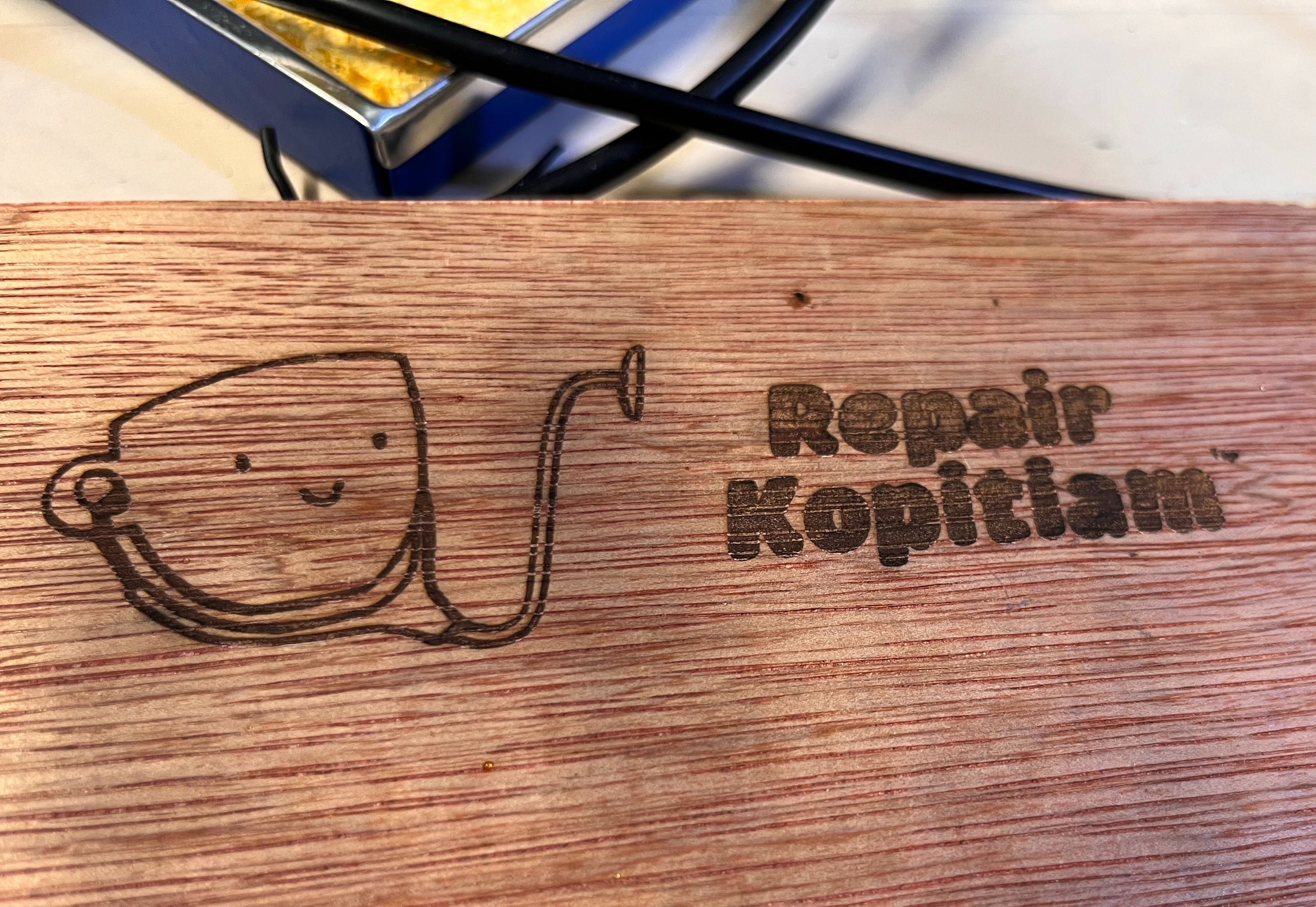 A wooden board with 'Repair Kopitiam' printed on it, and a coffee cup wearing a stethoscope
